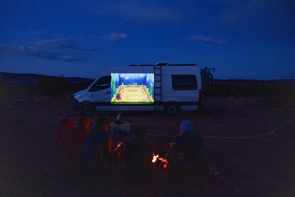 Mario Party is projected onto the side of a van and 4 people are playing games in the foreground.