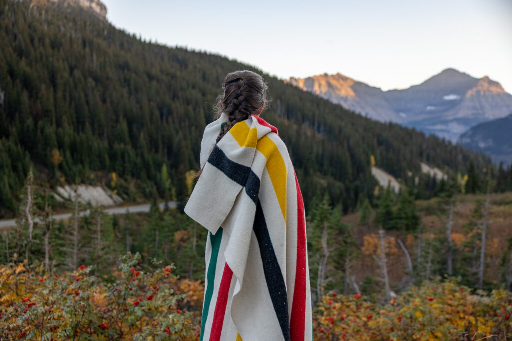 Woman wrapped in a blanket overlooking Glacier National Park mountains in the background.