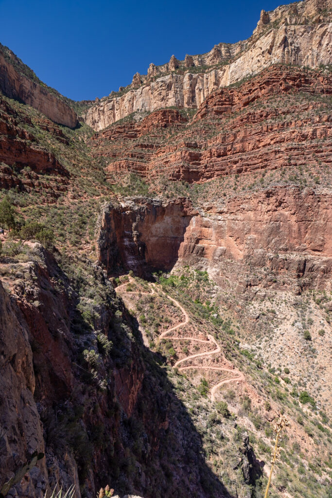 Switchbacks of the Bright Angel Trail descending into the Grand Canyon with layered red rock formations and sparse vegetation visible on the canyon walls