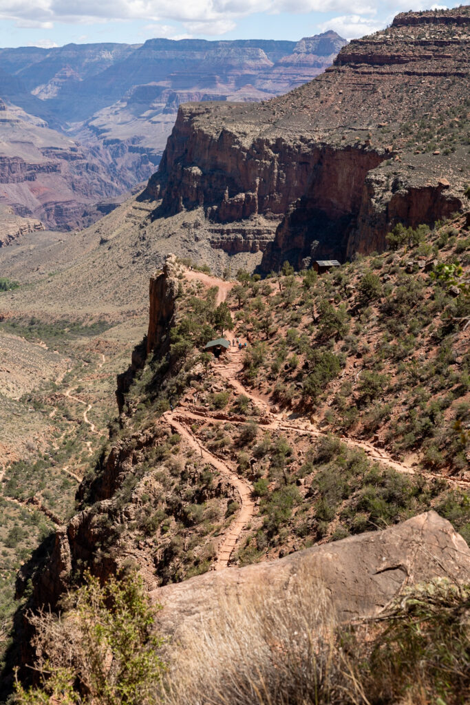 View of the Bright Angel Trail switchbacks descending into the Grand Canyon, with distinctive red rock formations and layered canyon walls visible in the distance. This is one of the best things to do at the Grand Canyon South Rim.