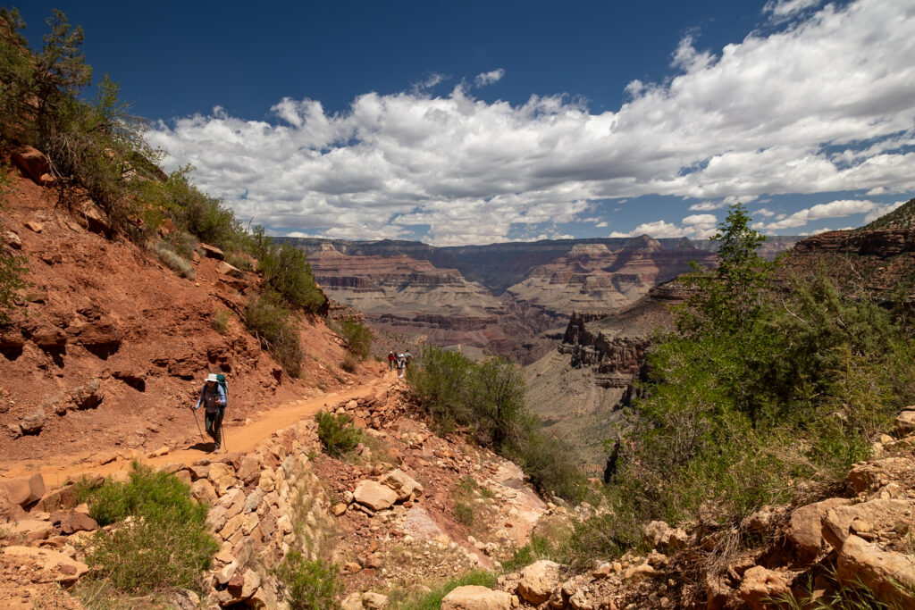 Hiker on the Bright Angel Trail descending into the Grand Canyon with layered rock formations and canyon views visible in the distance