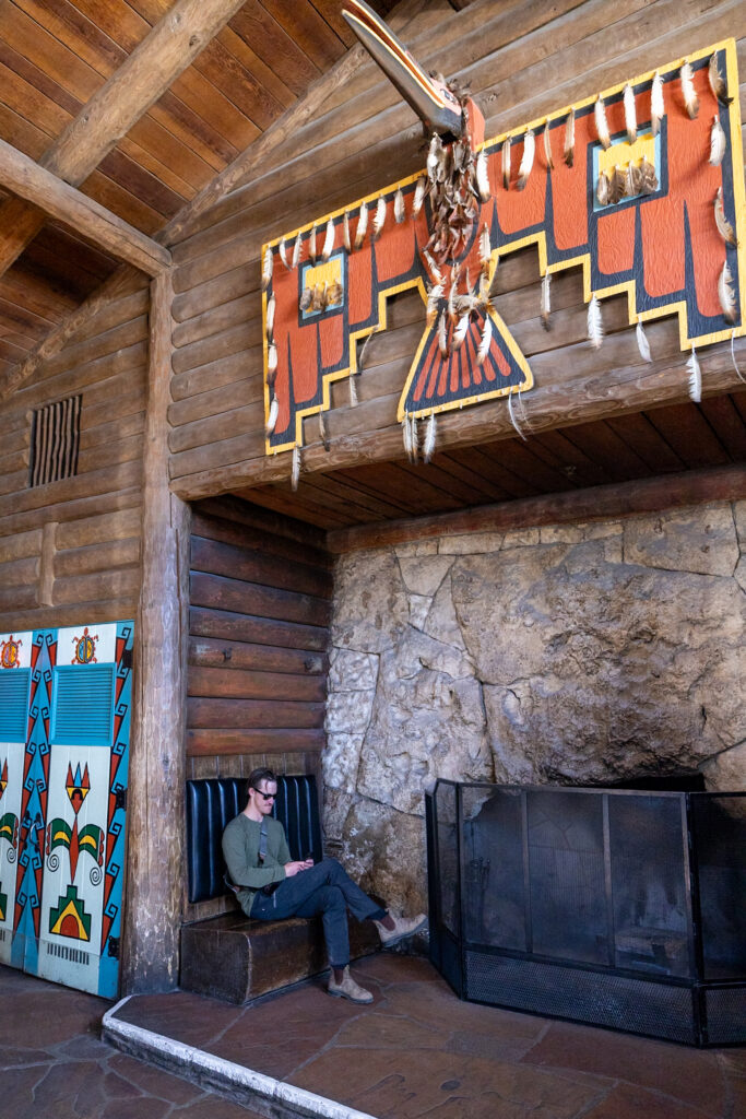 Elliot sitting in the historic interior of Bright Angel Lodge, with exposed wooden beams, Native American artwork, and a stone fireplace