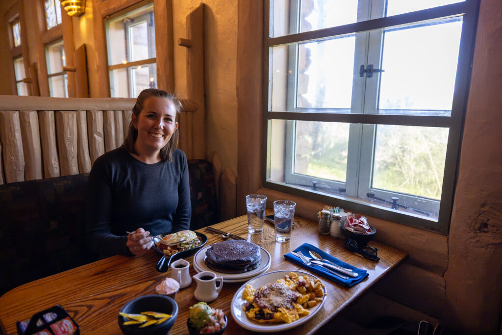 Jen dining at Harvey House Cafe with Grand Canyon views visible through the window behind her, showing the restaurant's historic interior and breakfast dishes