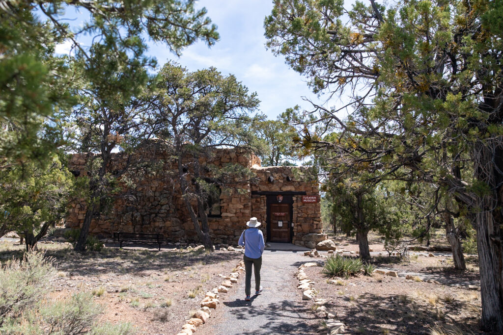 Jen approaching the Tusayan Puebloan Site, a stone structure built by ancestral Puebloans, surrounded by desert vegetation and pinyon-juniper forest along Desert View Drive. This is one of the best things to do in the Grand Canyon on the South Rim.