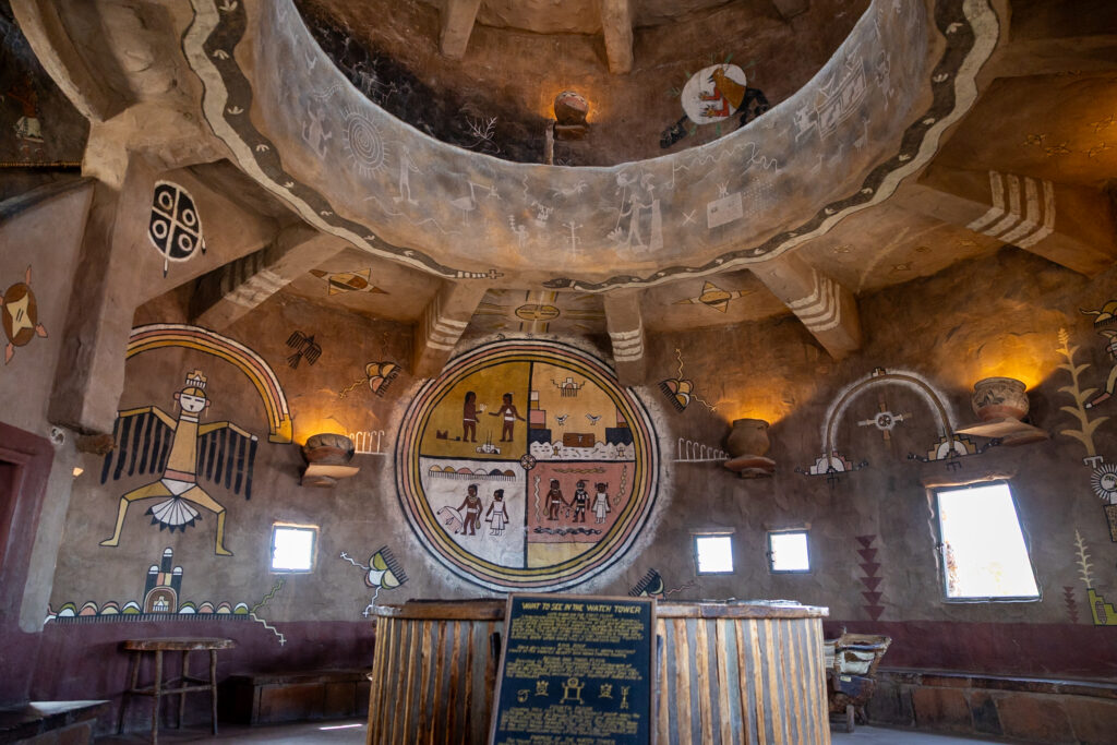 Interior of Desert View Watchtower showing Puebloan-inspired murals and designs on adobe walls, circular kiva structure above, and informational plaques below. This is one of the best things to do in the Grand Canyon on the South Rim.
