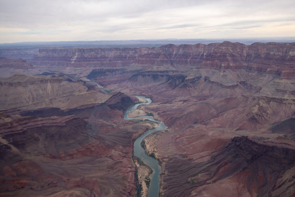 Aerial view of the Colorado River winding through the Grand Canyon's layered rock formations and plateaus under overcast sky