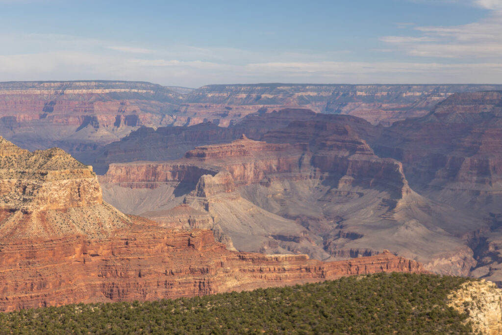 Aerial view from helicopter showing the South Rim in foreground with layered red rock formations and the North Rim visible across the canyon under clear sky