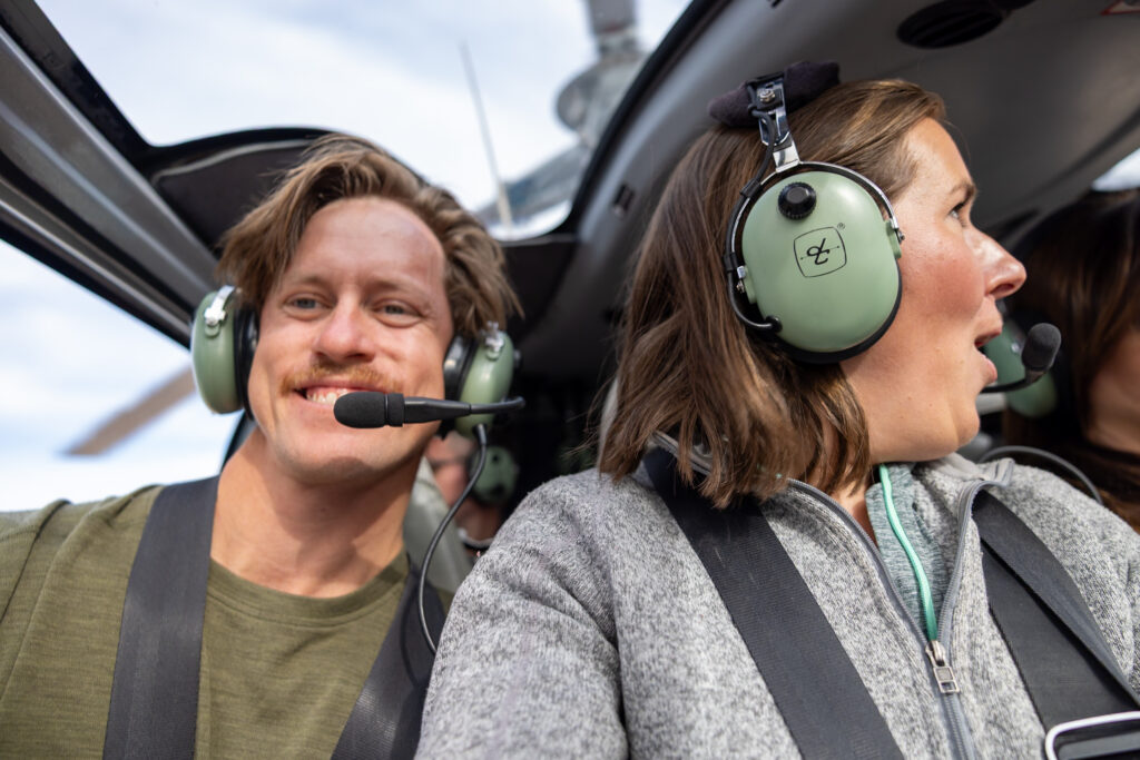 Two people wearing headsets inside a helicopter, smiling during their Grand Canyon tour flight