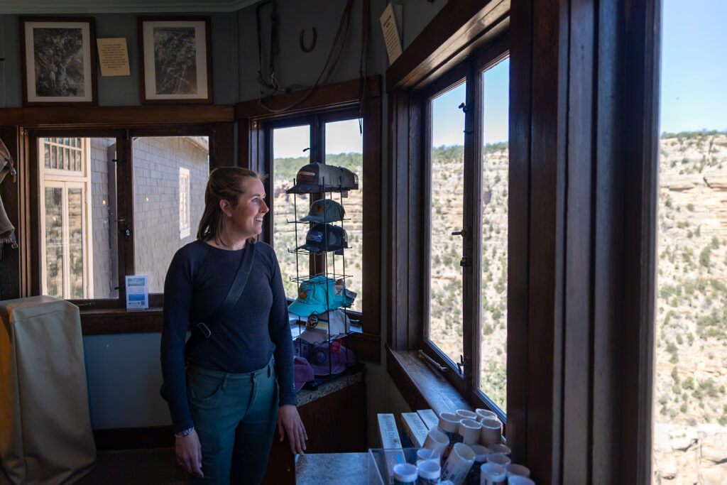 Jen standing inside Kolb Studio, a historic building in Grand Canyon Village, with large windows framing views of the canyon landscape and vintage photography equipment visible