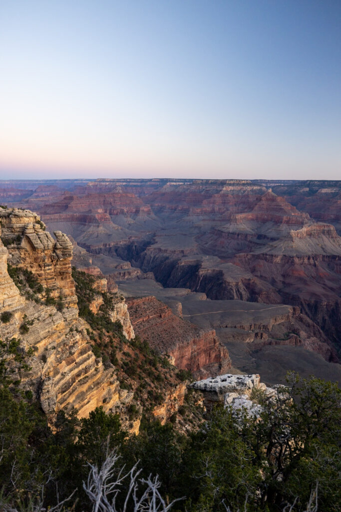 Grand Canyon South Rim's Mather Point at sunrise with layered rock formations and canyon depths illuminated by early morning light.