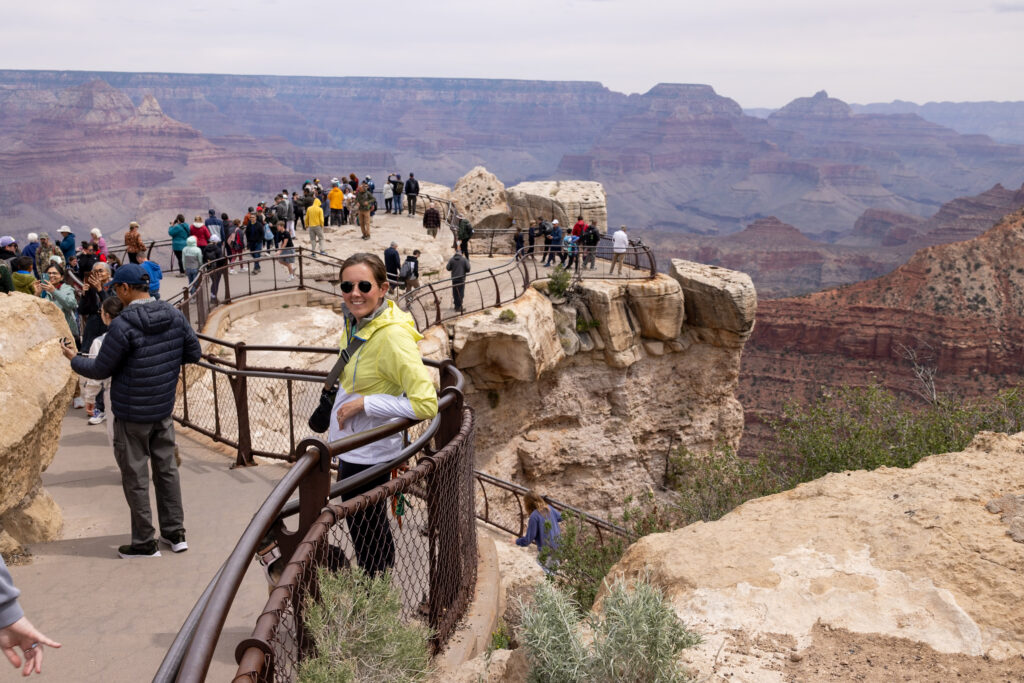 Visitors on a paved rim walkout (Mather Point) at Grand Canyon National Park, with layered canyon walls and rock formations visible in the background
