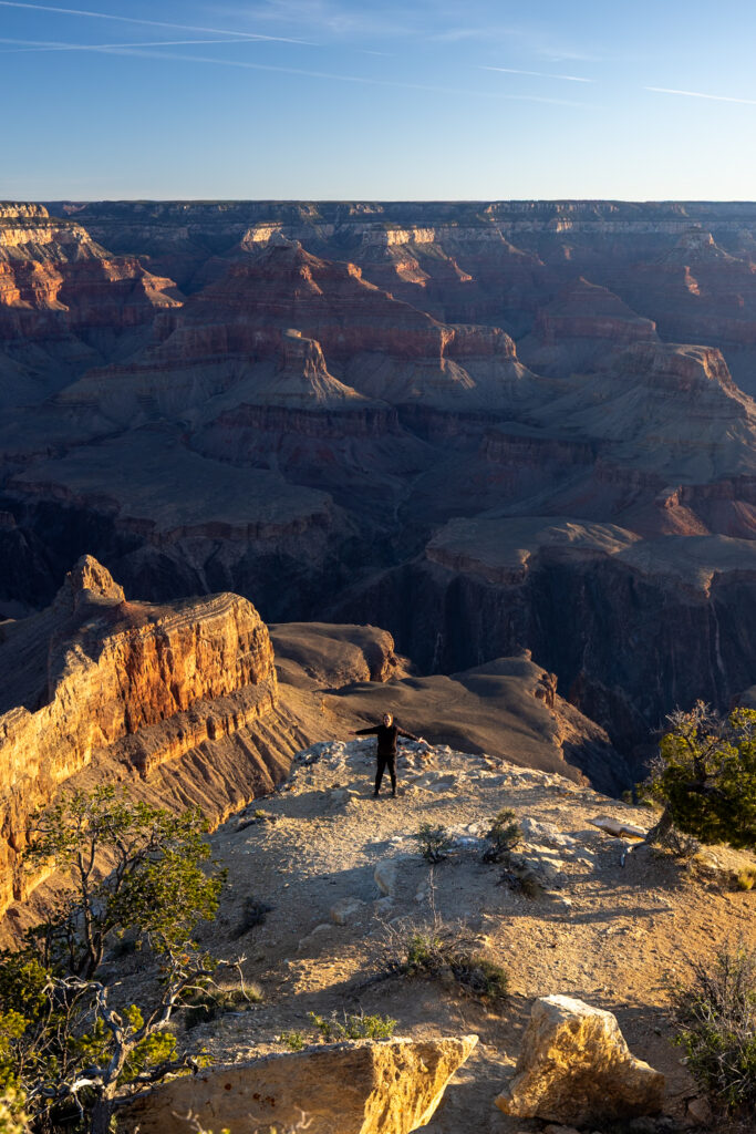 Hiker standing on a sunlit overlook at Powell Point with expansive views of the Grand Canyon's layered rock formations and deep valleys below