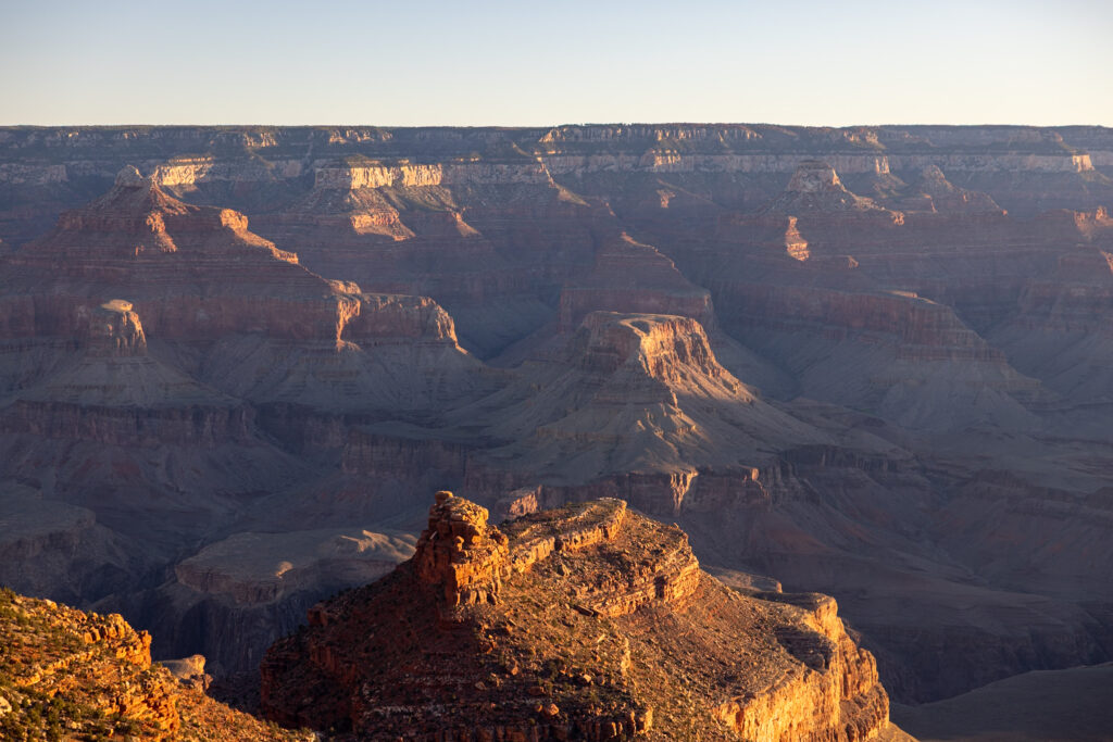 Expansive view of the Grand Canyon's layered rock formations and plateaus illuminated by golden sunlight from the South Rim near Grand Canyon Village