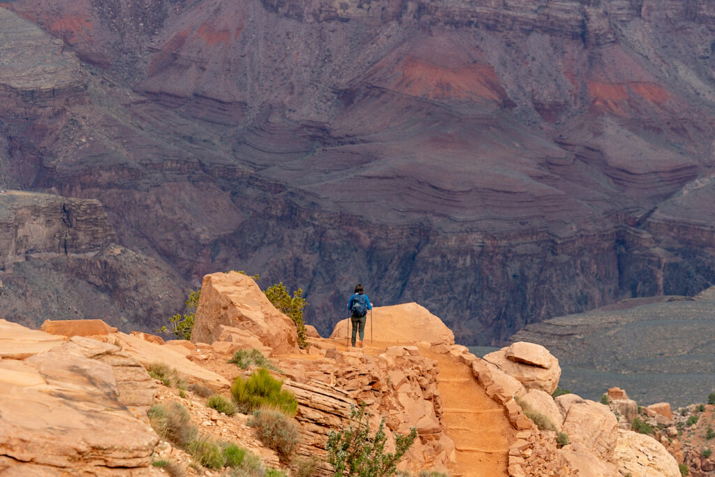 Hiker on the South Kaibab Trail with expansive canyon rock formations and layered geological strata visible in the background. This is one of the best things to do at the Grand Canyon South Rim.