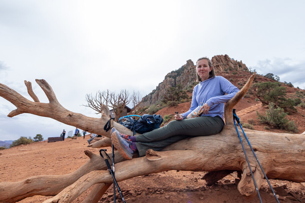 Jen resting on a fallen log at Cedar Ridge on the South Kaibab Trail, with canyon walls and hiking gear visible in the background