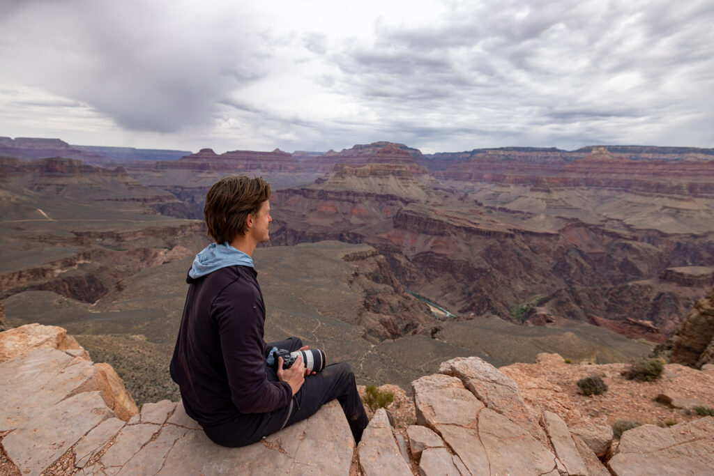 Elliot sitting on a rock outcrop at Skeleton Point on South Kaibab Trail, overlooking the expansive layered canyon walls and Colorado River below