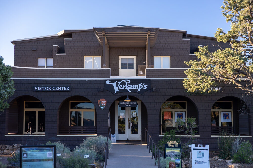 Century-old stone building with dark exterior, arched windows, and "Verkamp's" signage, functioning as a gift shop and museum in Grand Canyon Village. This is one of the best things to do on the Grand Canyon South Rim.