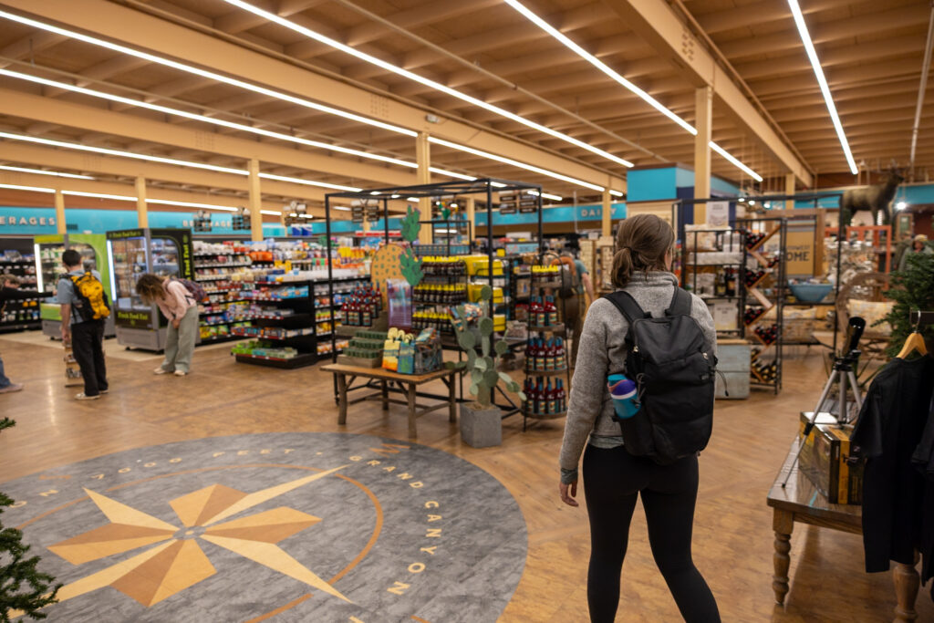 Interior of Canyon Village Market & Deli showing shelves of snacks and beverages, with visitors shopping and a decorative floor pattern