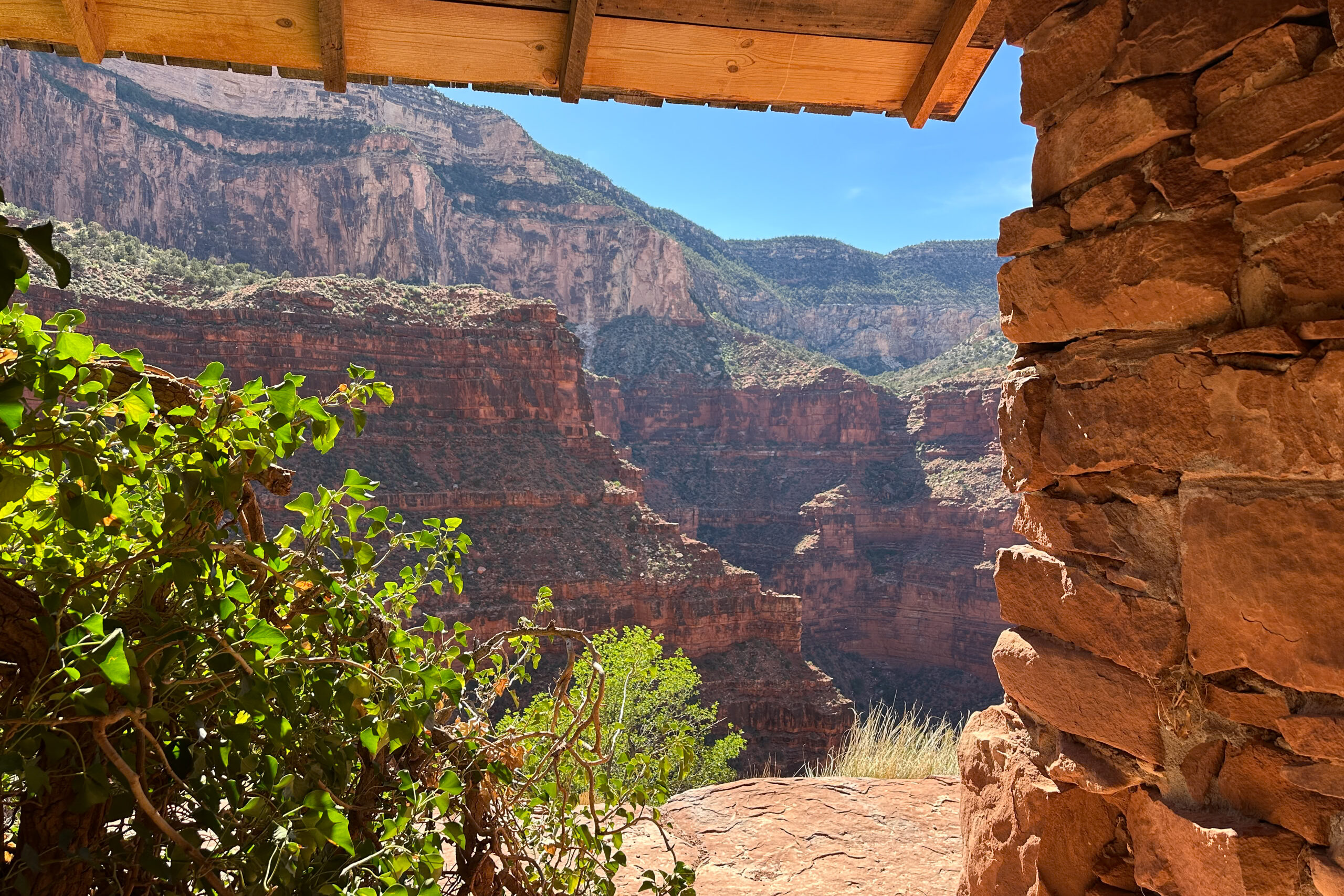 View of layered red canyon walls and side canyon from a shaded shelter with wooden beams at Santa Maria Spring on the Hermit Trail