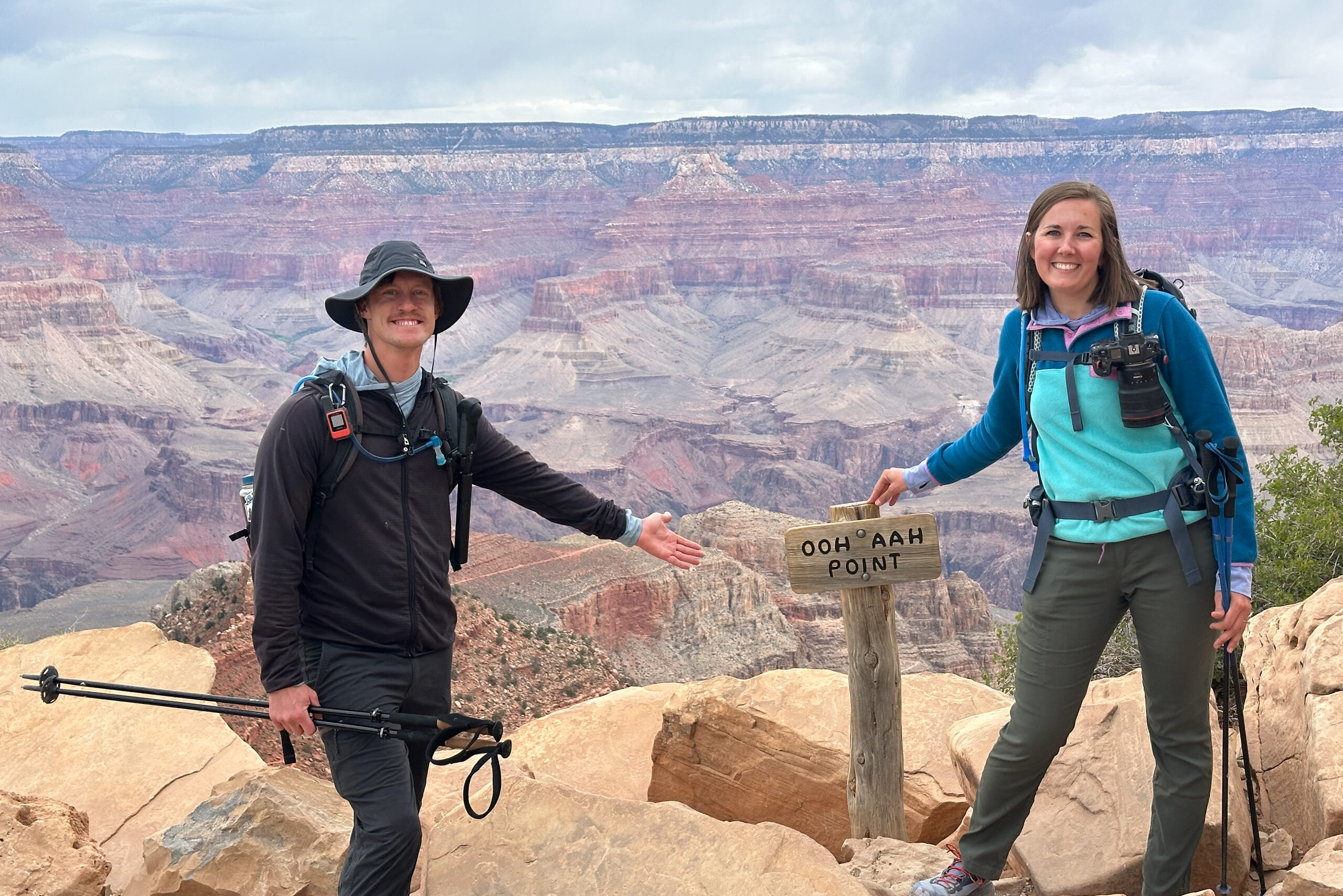 Two hikers posing at the Ooh Aah Point trail marker with the Grand Canyon landscape stretching behind them. This is one of the best things to do at the Grand Canyon South Rim.