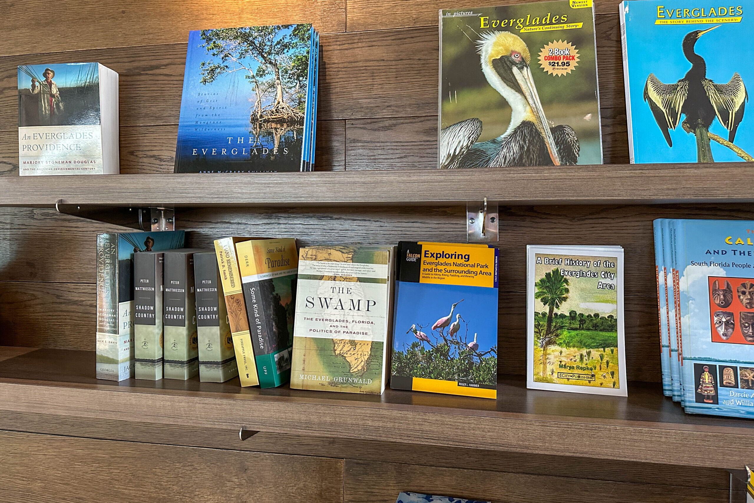 Collection of Everglades-related books and guides displayed on wooden shelves, including titles about the Everglades, wildlife field guides, and regional history books