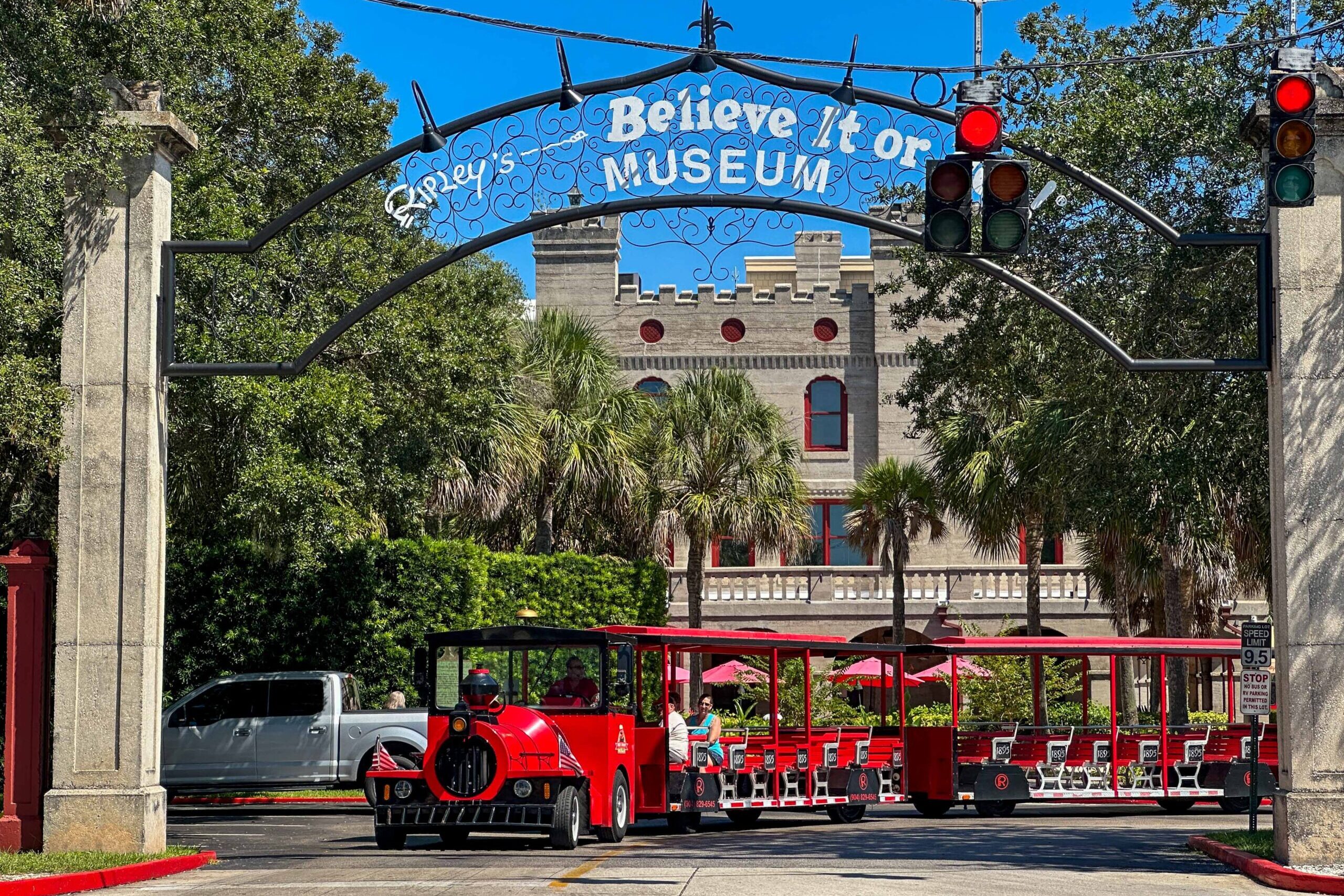 Bright red train-style trolley with passengers stopped under Ripley's Believe It or Not Museum archway in St. Augustine, with historic castle-like building visible behind palm trees