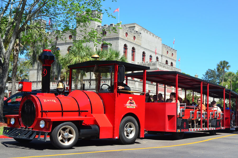 Bright red Ripley's Red Train trolley with passengers aboard, passing historic buildings and palm trees in St. Augustine