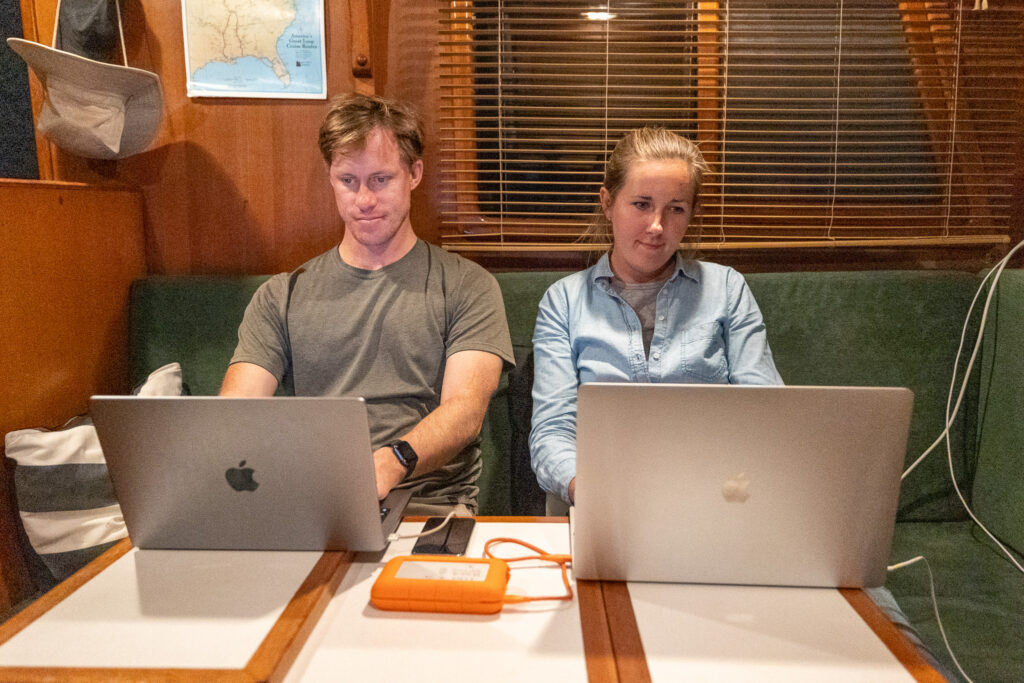 Jen and Elliot working with their laptops open in their boat