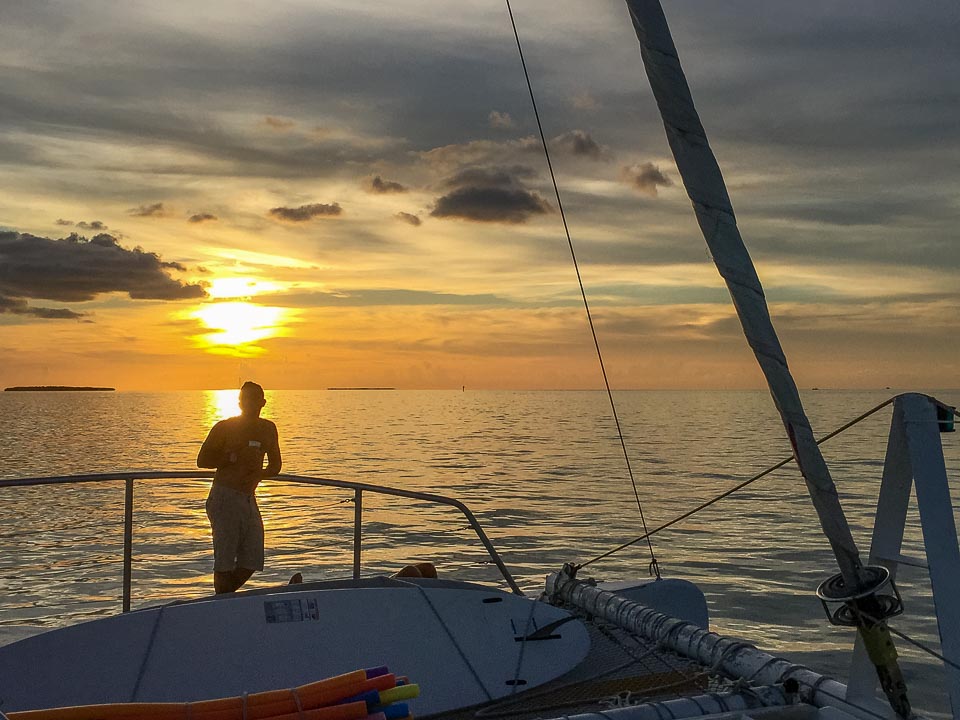 Man standing on a boat after snorkeling in Florida with the sun setting behind him.