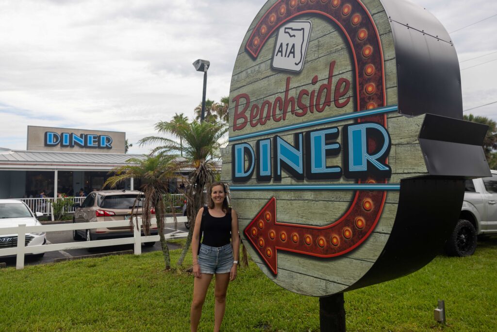 Jen standing in front of the Beachside Diner's vintage neon sign, with the diner building visible in the background